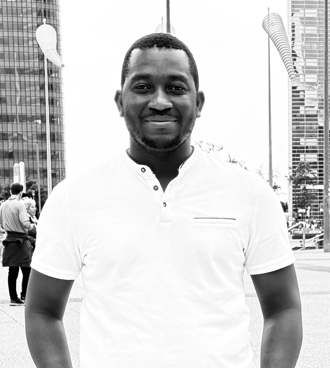 Black and white candid photo of Kwamivi Gomado smiling outdoors.